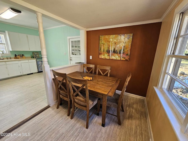 dining area with ornamental molding, light wood-type flooring, decorative columns, and wood walls