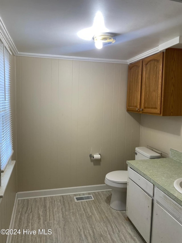 bathroom featuring hardwood / wood-style floors, wood walls, toilet, crown molding, and vanity