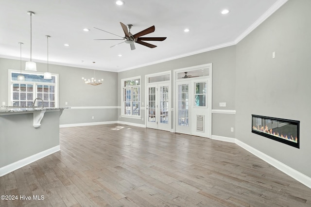 unfurnished living room featuring ceiling fan with notable chandelier, sink, wood-type flooring, and crown molding