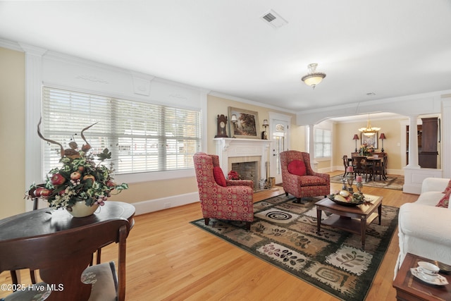 living room with decorative columns, light hardwood / wood-style flooring, ornamental molding, and an inviting chandelier