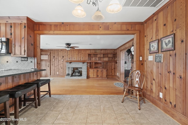 interior space with decorative backsplash, a brick fireplace, ceiling fan, light tile patterned floors, and hanging light fixtures