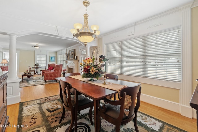 dining room featuring a notable chandelier, light hardwood / wood-style floors, crown molding, and decorative columns