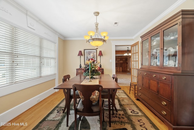 dining space with light wood-type flooring, crown molding, and a notable chandelier