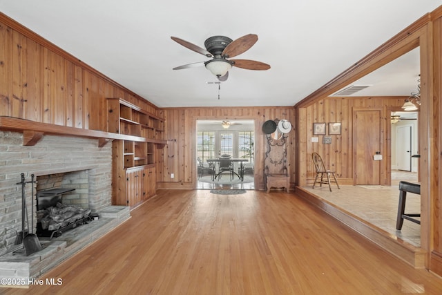 unfurnished living room featuring a brick fireplace, ceiling fan, wooden walls, and light hardwood / wood-style flooring