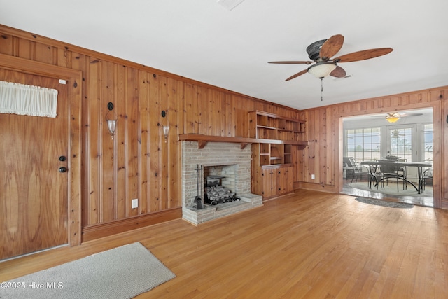 living room featuring ceiling fan, wood-type flooring, wooden walls, and a brick fireplace