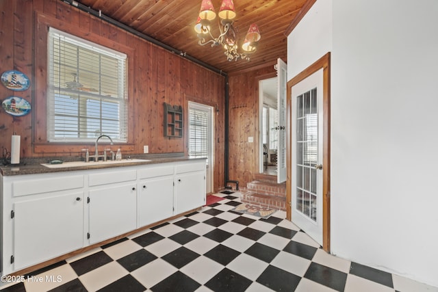 kitchen featuring sink, wooden ceiling, a notable chandelier, wooden walls, and white cabinets