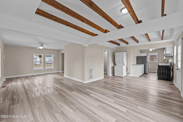 unfurnished living room featuring beamed ceiling, stacked washing maching and dryer, light wood-style flooring, and baseboards