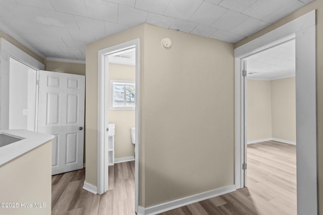 corridor featuring crown molding, baseboards, and wood finished floors