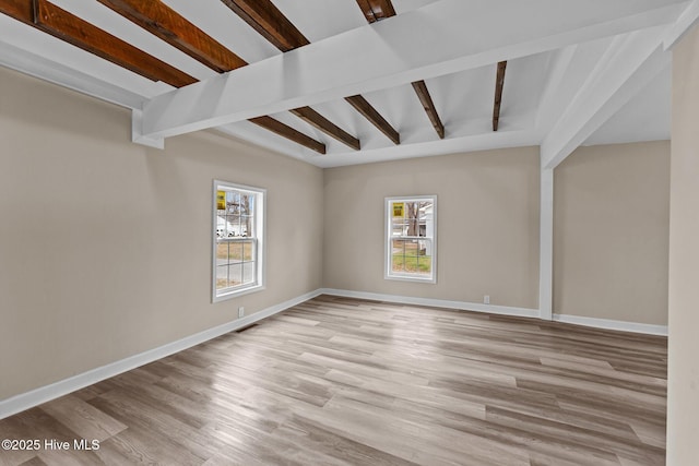 empty room featuring light wood-style floors, visible vents, baseboards, and beamed ceiling