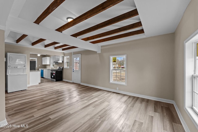 unfurnished living room with baseboards, light wood-style floors, beamed ceiling, and stacked washer / drying machine