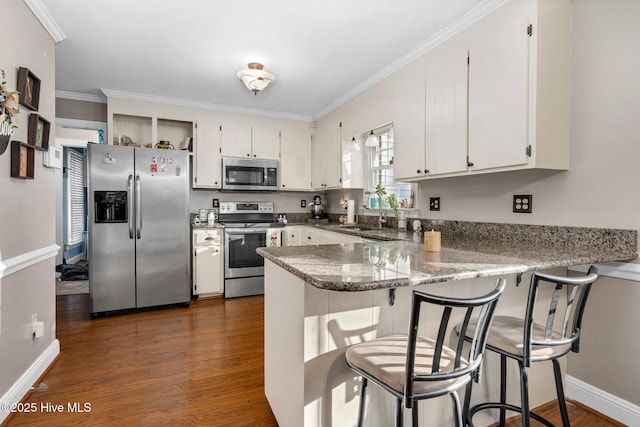 kitchen with dark wood-type flooring, dark stone counters, white cabinets, kitchen peninsula, and stainless steel appliances