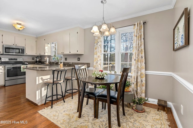 kitchen featuring dark stone counters, hardwood / wood-style flooring, kitchen peninsula, stainless steel appliances, and a chandelier