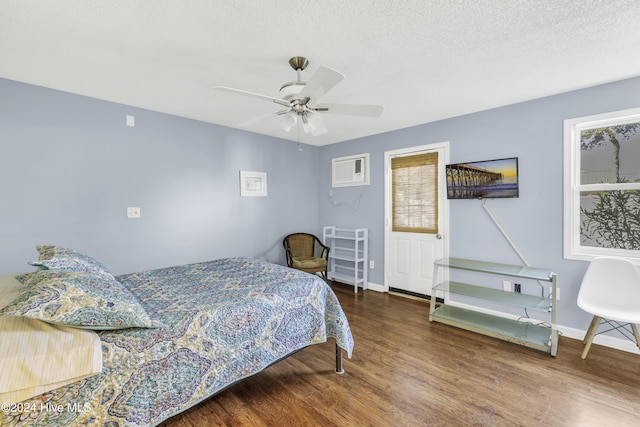 bedroom with a wall mounted air conditioner, a ceiling fan, a textured ceiling, wood finished floors, and baseboards