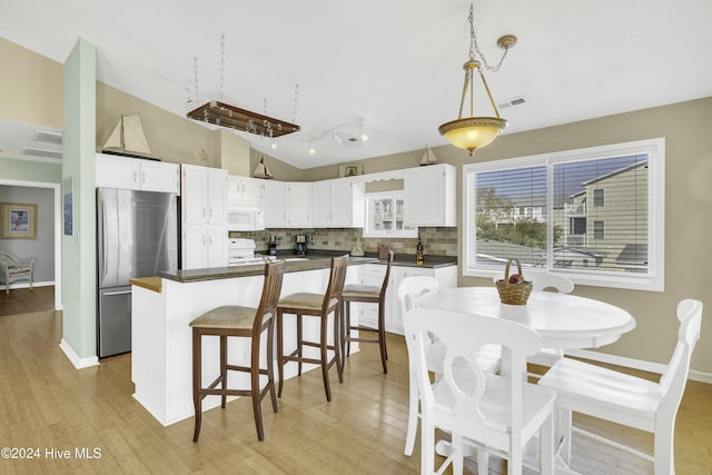 kitchen with lofted ceiling, white cabinets, hanging light fixtures, light hardwood / wood-style flooring, and stainless steel refrigerator