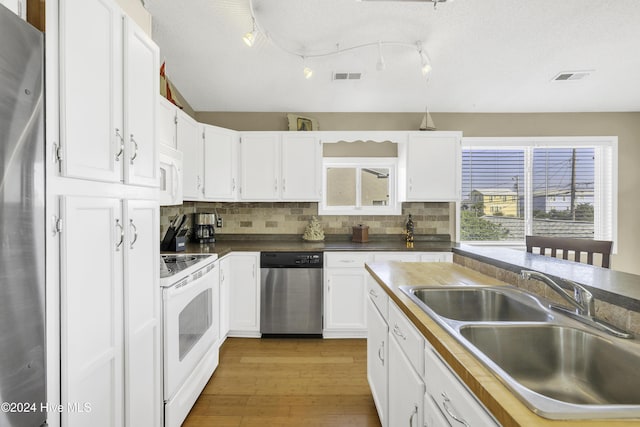 kitchen with light wood-type flooring, backsplash, stainless steel appliances, sink, and white cabinetry