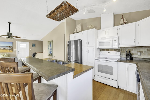 kitchen featuring white appliances, vaulted ceiling, dark countertops, and a sink