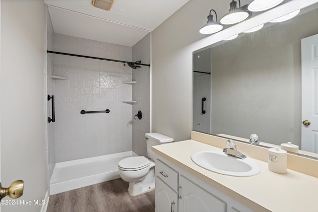 bathroom featuring hardwood / wood-style flooring, vanity, toilet, and tiled shower