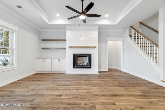 unfurnished living room with light wood finished floors, stairway, and a raised ceiling