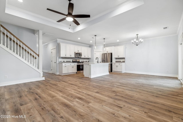 unfurnished living room featuring light wood finished floors, stairway, a raised ceiling, and crown molding