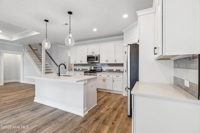 kitchen with white cabinets, a kitchen island with sink, stainless steel appliances, light countertops, and pendant lighting