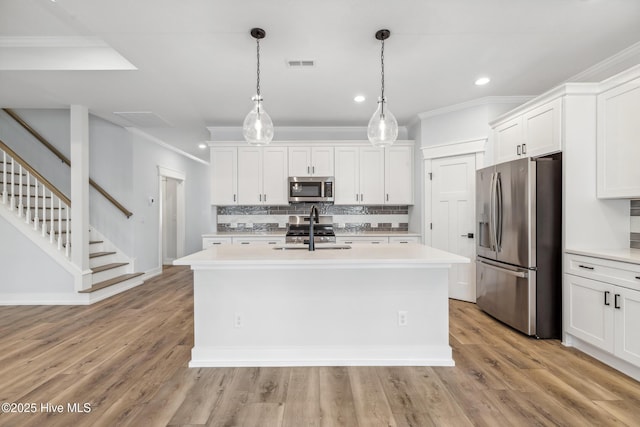 kitchen featuring decorative light fixtures, light countertops, appliances with stainless steel finishes, white cabinetry, and a sink