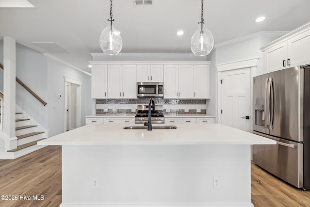 kitchen featuring stainless steel appliances, light countertops, a center island with sink, and decorative light fixtures