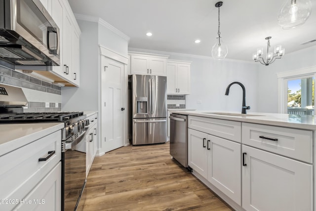 kitchen featuring decorative light fixtures, light countertops, appliances with stainless steel finishes, white cabinetry, and a sink