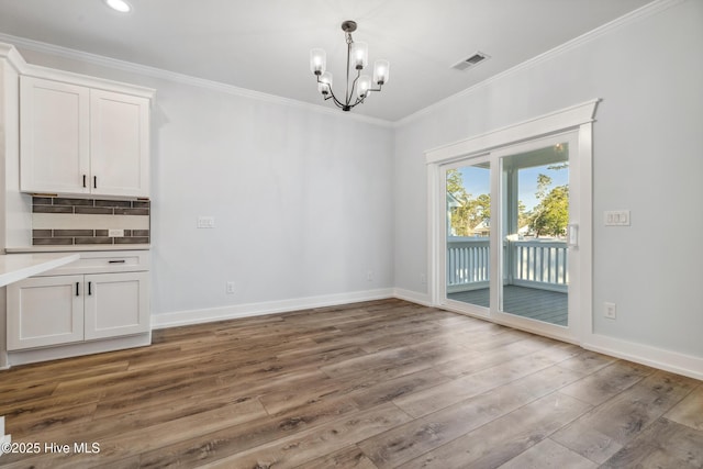 unfurnished dining area with wood finished floors, visible vents, baseboards, ornamental molding, and an inviting chandelier