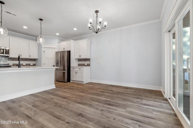 kitchen featuring white cabinets, ornamental molding, hanging light fixtures, stainless steel appliances, and light countertops