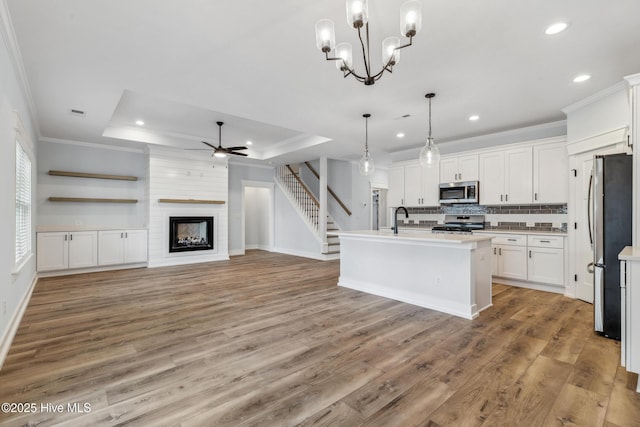 kitchen featuring decorative light fixtures, stainless steel appliances, light countertops, white cabinets, and an island with sink