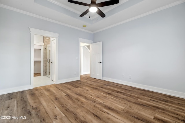 unfurnished bedroom with wood finished floors, baseboards, a tray ceiling, ensuite bath, and crown molding