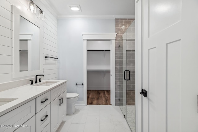 bathroom with double vanity, a walk in closet, crown molding, a shower stall, and a sink