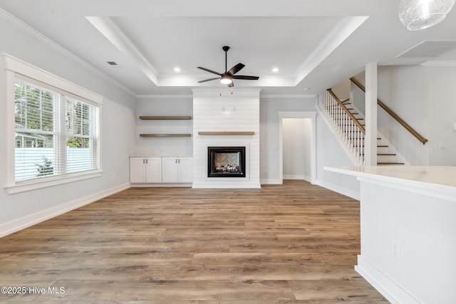 unfurnished living room featuring a large fireplace, a tray ceiling, wood finished floors, and ornamental molding