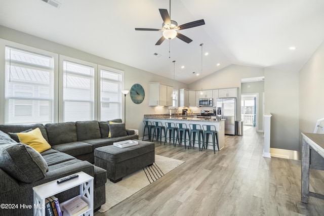 living room with light hardwood / wood-style flooring, vaulted ceiling, ceiling fan, and a healthy amount of sunlight