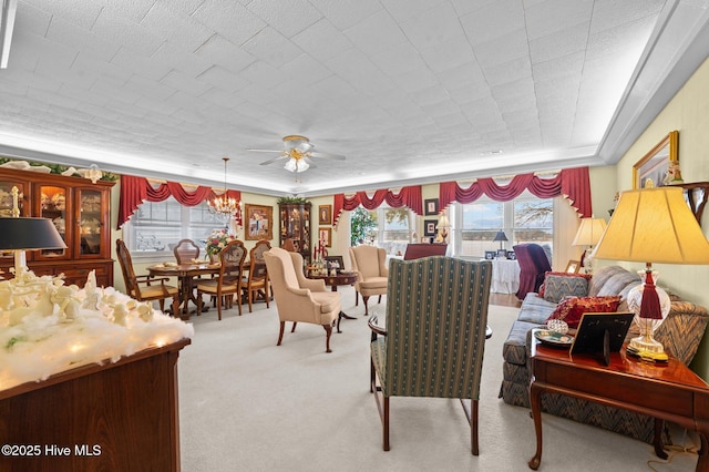 living room featuring a raised ceiling, light colored carpet, and ceiling fan with notable chandelier