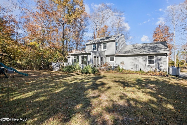 back of property with central AC unit, a playground, and a yard