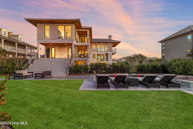 back house at dusk with a lawn, a balcony, and a patio