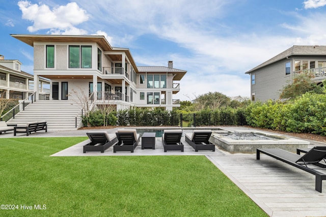 back of property featuring a swimming pool with hot tub, a balcony, a patio area, and a lawn