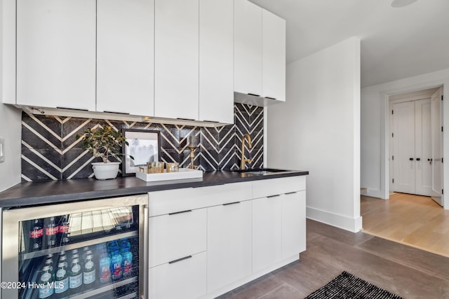 interior space with backsplash, white cabinets, sink, dark hardwood / wood-style flooring, and beverage cooler