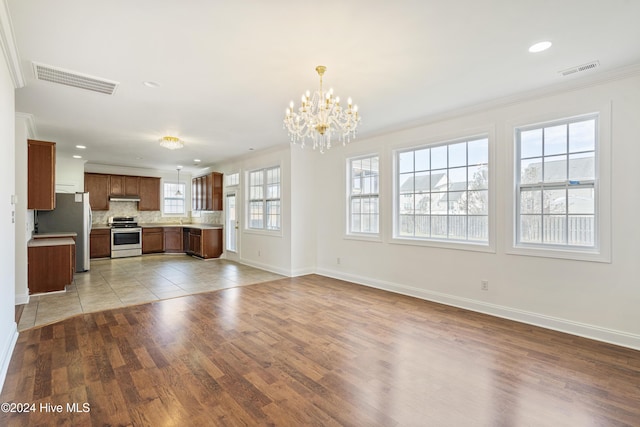 unfurnished living room with crown molding, a chandelier, and light wood-type flooring