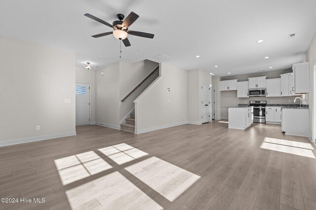 kitchen with white cabinetry, dark stone counters, a center island, stainless steel appliances, and light wood-type flooring