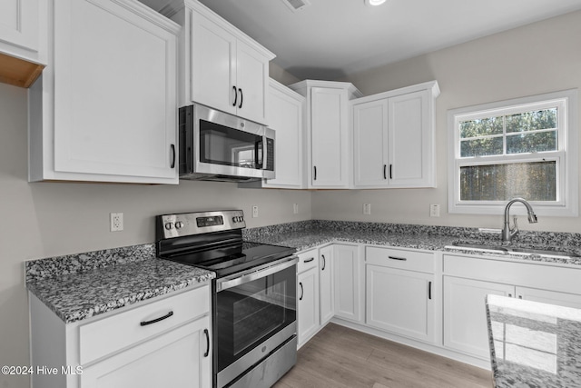 kitchen featuring light stone countertops, stainless steel appliances, light wood-style floors, white cabinetry, and a sink