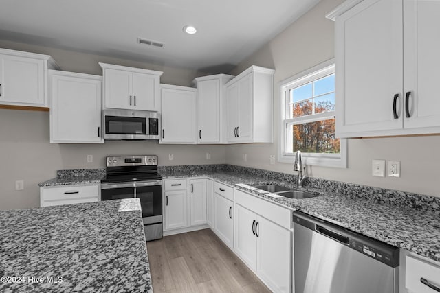 kitchen featuring visible vents, appliances with stainless steel finishes, white cabinets, a sink, and dark stone counters