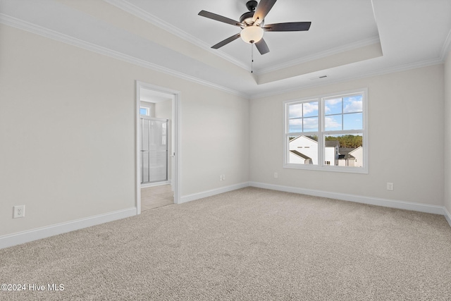 empty room with ceiling fan, light colored carpet, baseboards, a raised ceiling, and crown molding