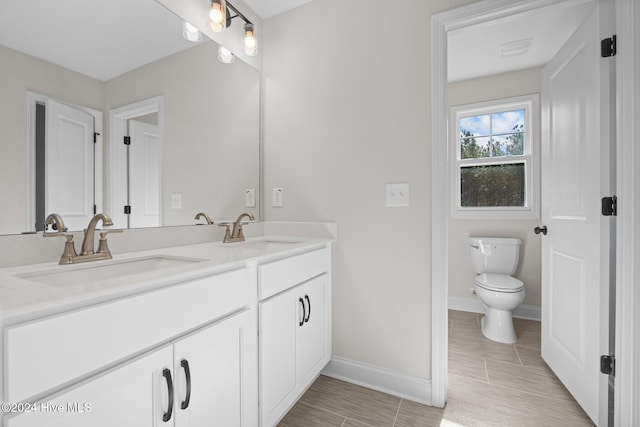 full bath with baseboards, a sink, toilet, and double vanity