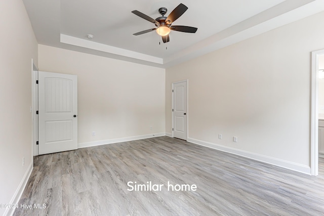 spare room with light wood-type flooring, a tray ceiling, and ceiling fan