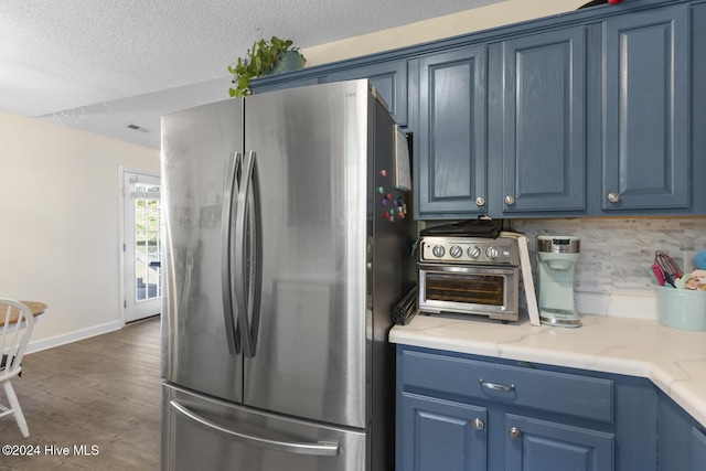 kitchen with backsplash, blue cabinetry, stainless steel refrigerator, and dark wood-type flooring