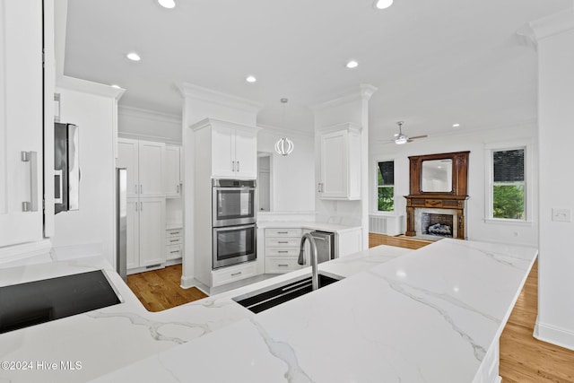 kitchen with decorative light fixtures, sink, white cabinets, double oven, and light stone counters