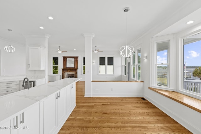 kitchen with decorative light fixtures, white cabinets, light stone countertops, and ornamental molding