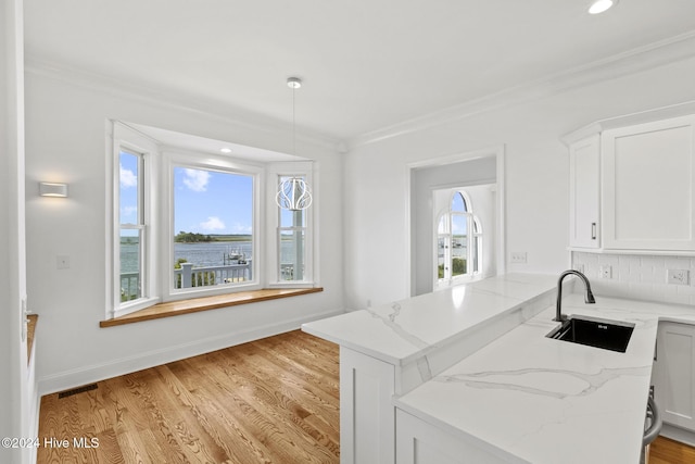 kitchen featuring light stone countertops, white cabinetry, kitchen peninsula, and sink